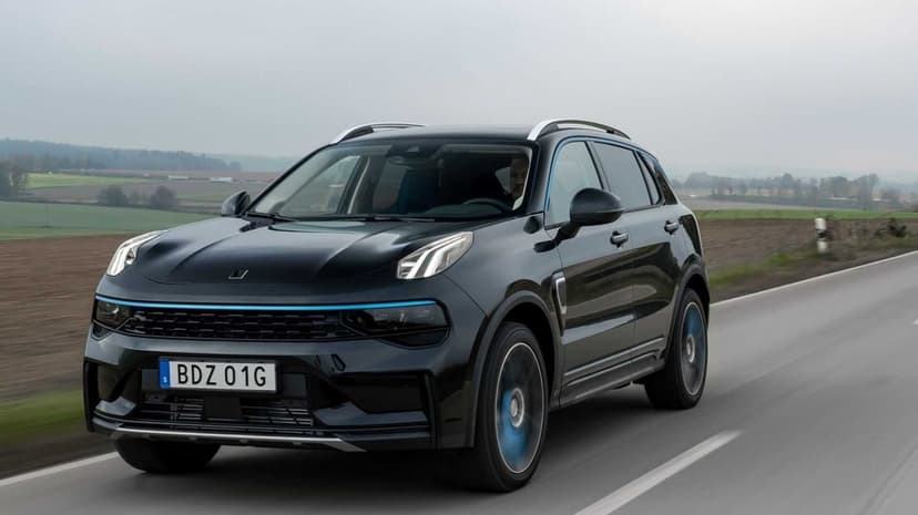 Black Lynk & Co 01 SUV with blue accents driving on a paved road through a misty rural field landscape.