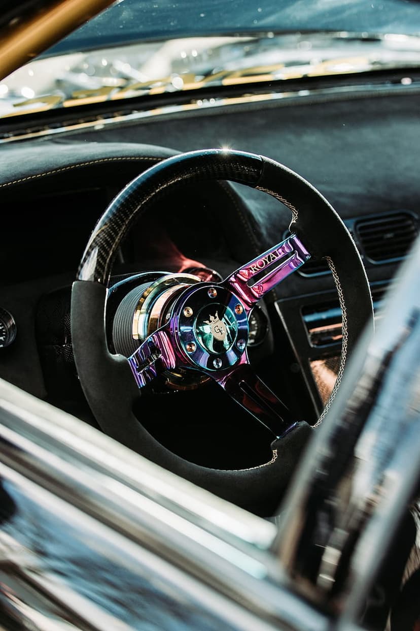 Carbon fiber steering wheel featuring a vibrant iridescent hub and metallic bolts in a dark vehicle cabin.