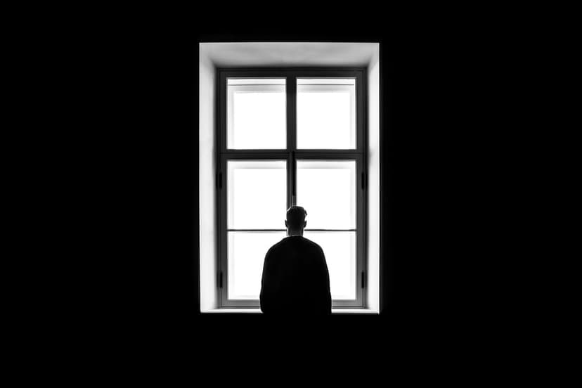 Person in silhouette stands before a bright rectangular window with dark shadows creating a high-contrast scene.