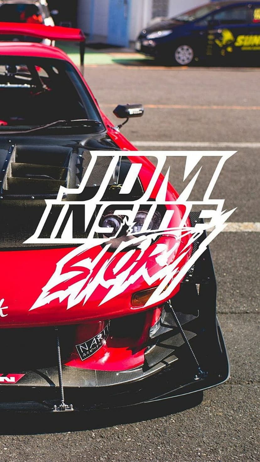 Red JDM sports car with white stickers on a race track featuring a large hood scoop and aggressive bumper.