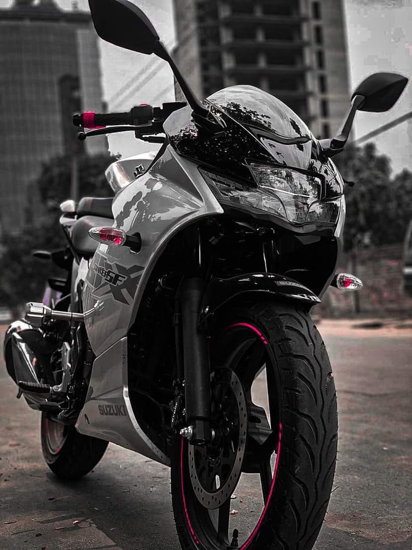 Silver Suzuki Gixxer SF sportbike with red rim accents and LED lights parked on an urban street at a low angle.