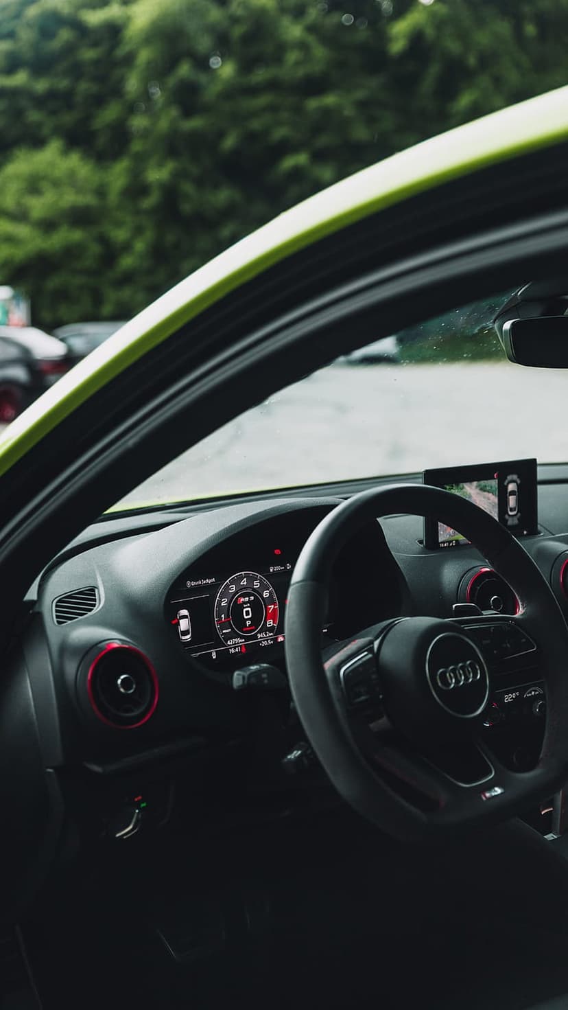 Audi steering wheel and digital dashboard with red ambient lighting from the driver's perspective.