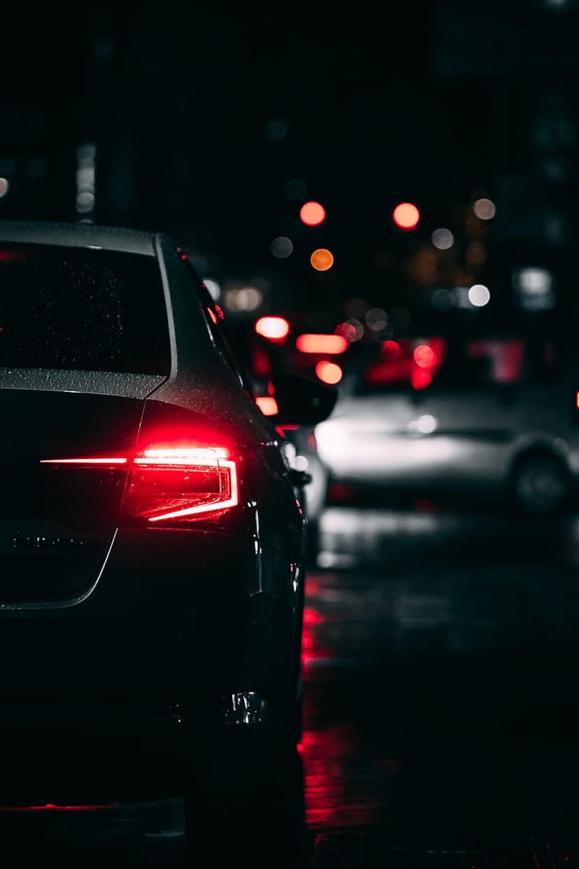 Red car taillight reflects on a rain-slicked city street with blurred bokeh lights in the distance.