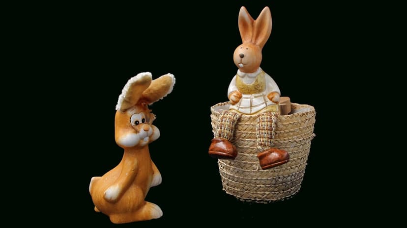 Orange ceramic rabbit and a bunny in a wicker basket stand against a solid black background in sharp focus.