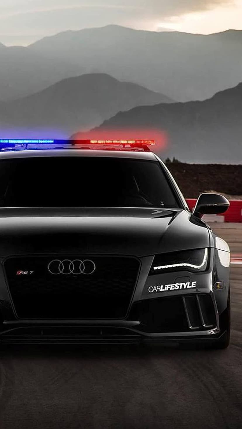 Black Audi RS7 police car with a lit roof bar parked on a mountain road under a dramatic, moody sky.