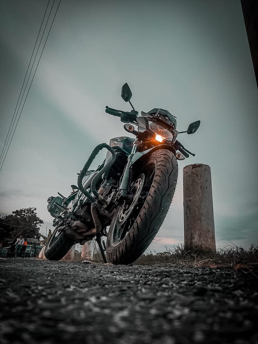 Cruiser motorcycle with a glowing headlight parked on a gravel roadside under a dramatic, dark overcast sky.