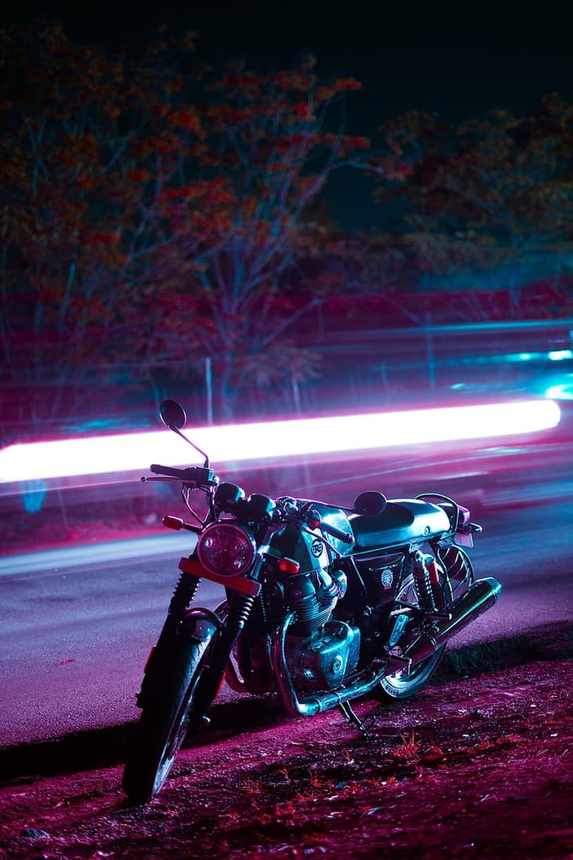 Classic motorcycle parked on an urban street at night with glowing pink and blue neon light trails behind it.