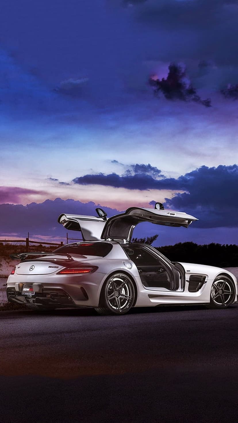 Mercedes-Benz SLS AMG with gullwing doors open on a road during a vibrant purple and blue sunset at twilight.