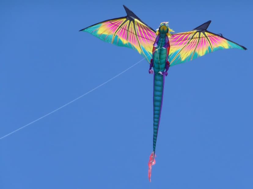 Vibrant dragon kite with yellow and pink wings flies against a clear blue sky during a sunny outdoor festival.