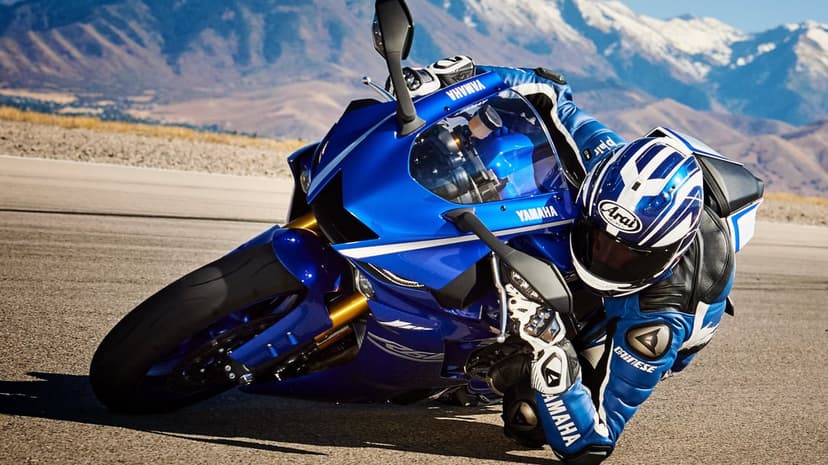 Blue Yamaha sportbike leaning deep into a turn on a racetrack with snow-capped mountains in the background.