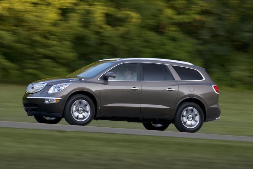 Bronze Buick Enclave SUV driving on a road with blurred green trees in the background during daylight.