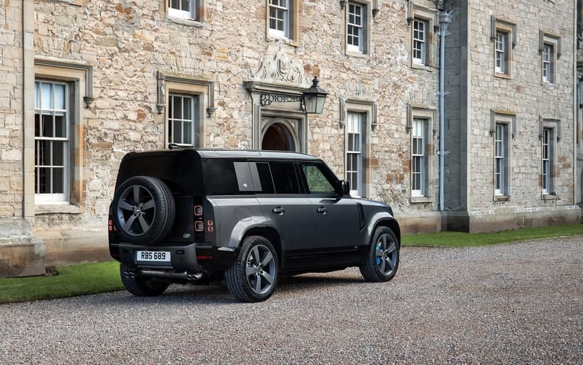 Dark grey Land Rover Defender SUV parked on a gravel path in front of a historic stone manor house facade.