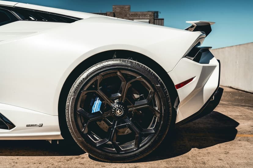 White Lamborghini Huracan rear quarter showing a black multi-spoke wheel, blue brake caliper, and spoiler.
