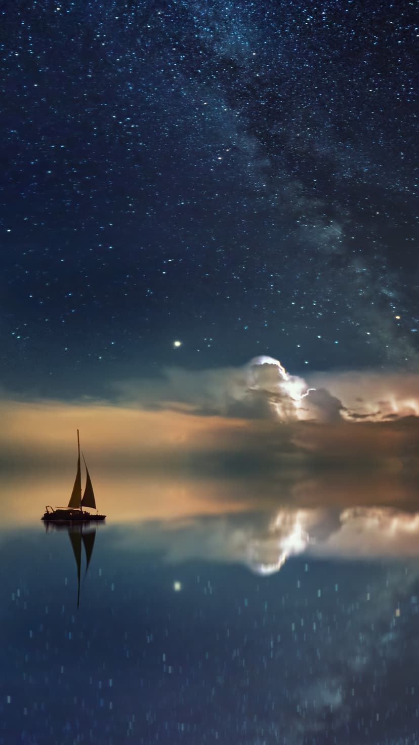 Lone sailboat rests on glass-like water reflecting a glowing nebula and a dense field of stars in the night sky.