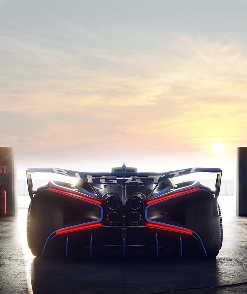 Bugatti Bolide rear with X-shaped taillights and quad exhaust pipes parked in a pit lane during sunrise.