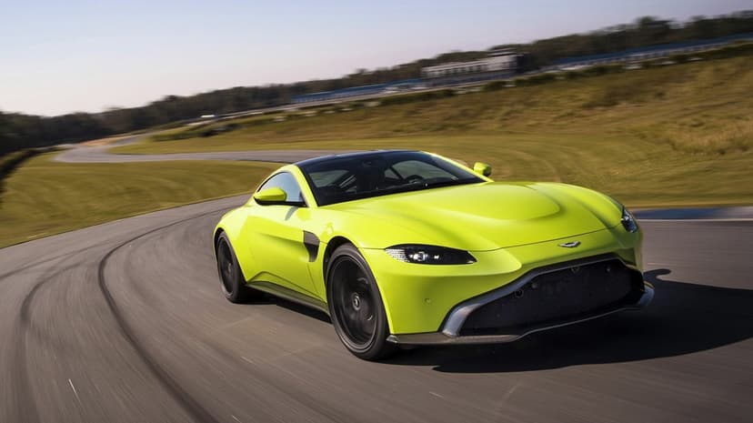 Lime green Aston Martin Vantage racing on a paved track with motion-blurred wheels under a clear sky.