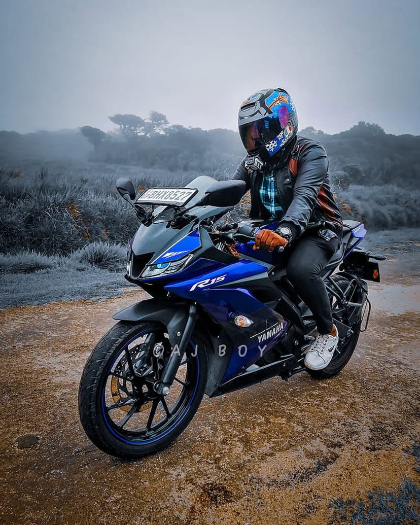 Rider on a blue Yamaha R15 motorcycle travels through a foggy forest landscape along a hazy mountain road.