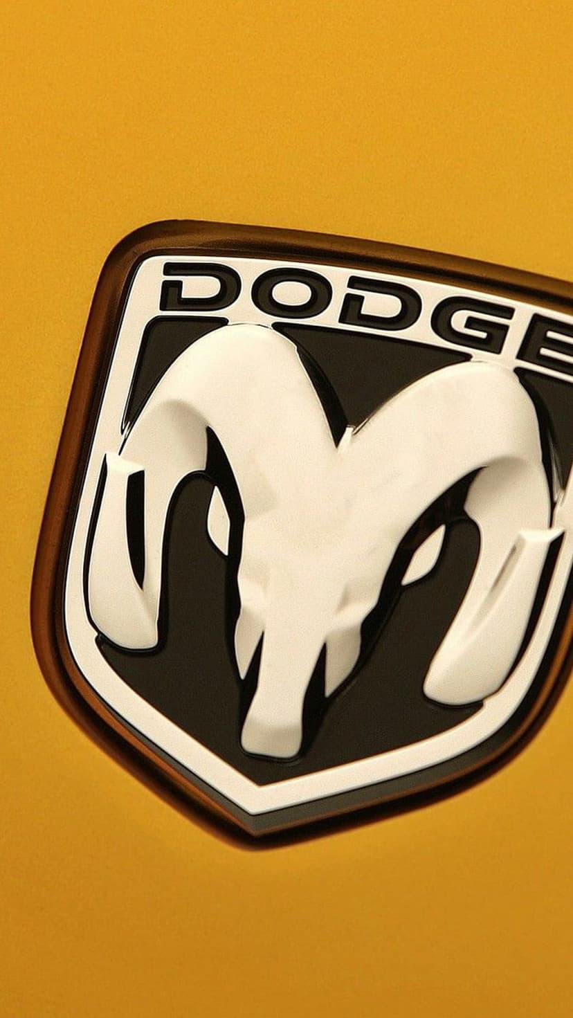 White ram head emblem inside a black and brown shield on a bright yellow car exterior in a macro close-up shot.