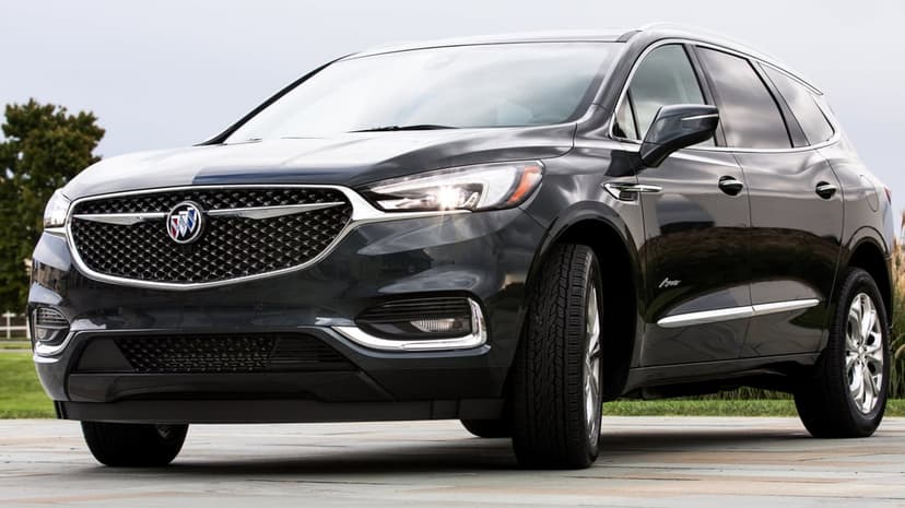Black Buick Enclave Avenir SUV with a chrome mesh grille and glowing headlights parked on stone pavement.