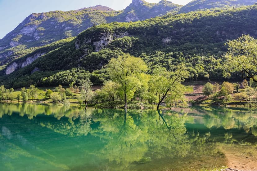 Turquoise alpine lake mirroring emerald green mountains and a clear sky in a vertical landscape composition.