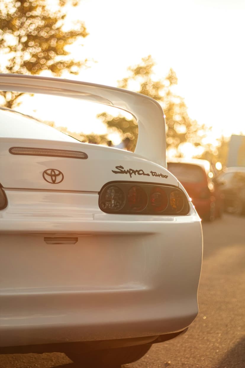Toyota Supra rear spoiler and circular taillights catch golden hour light against a blurry tree line.