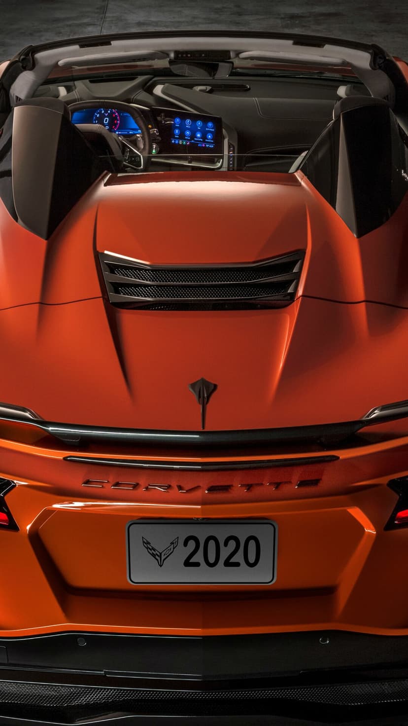 Rear view of an orange 2020 Corvette C8 Convertible showing the engine vents, logo, and digital dashboard.