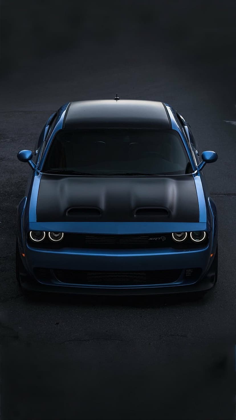 Blue Dodge Challenger Hellcat Widebody with black hood and halo headlights sits on dark asphalt road surface.