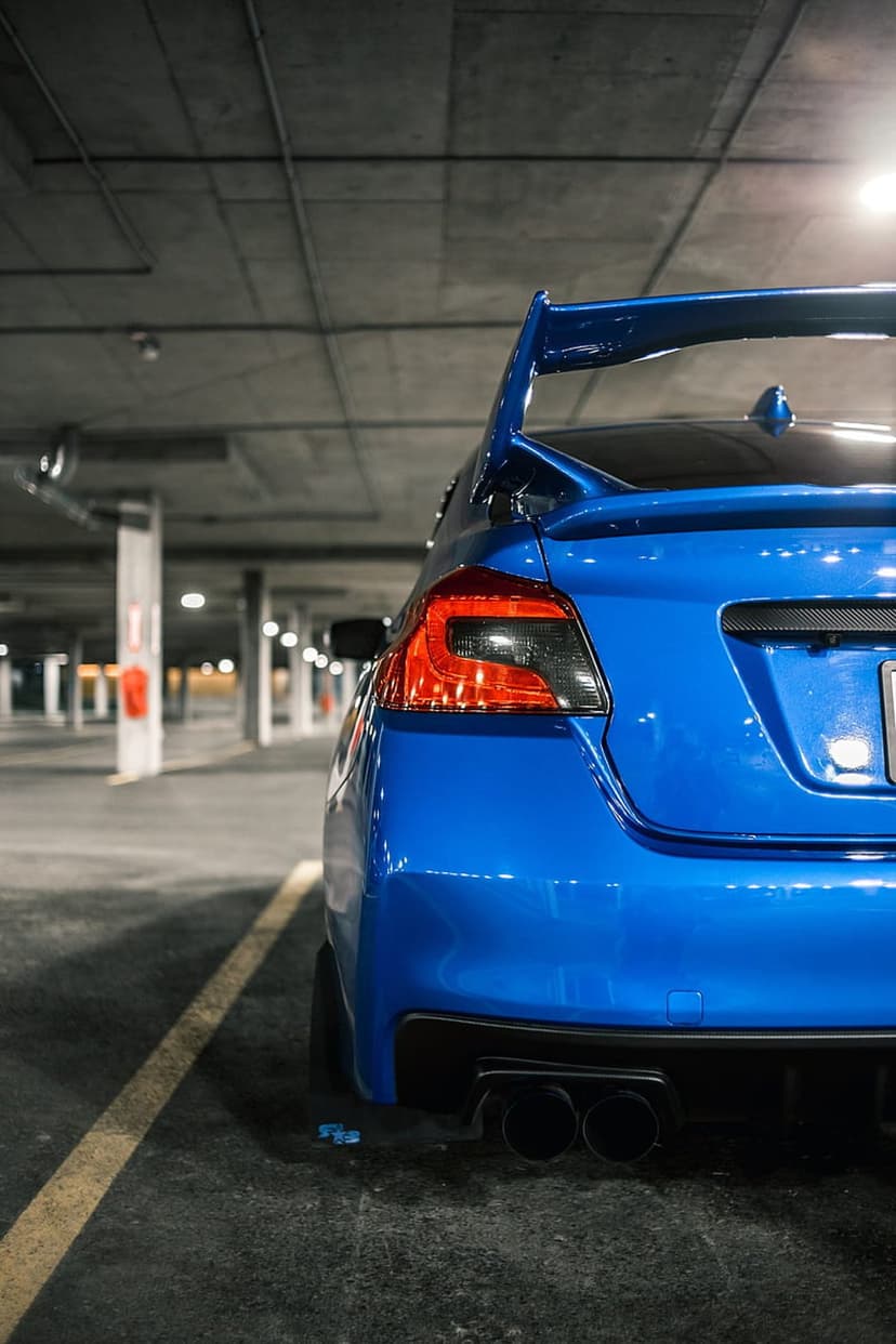 Subaru WRX STI rear wing and glowing taillights in a dark concrete garage with moody industrial lighting.