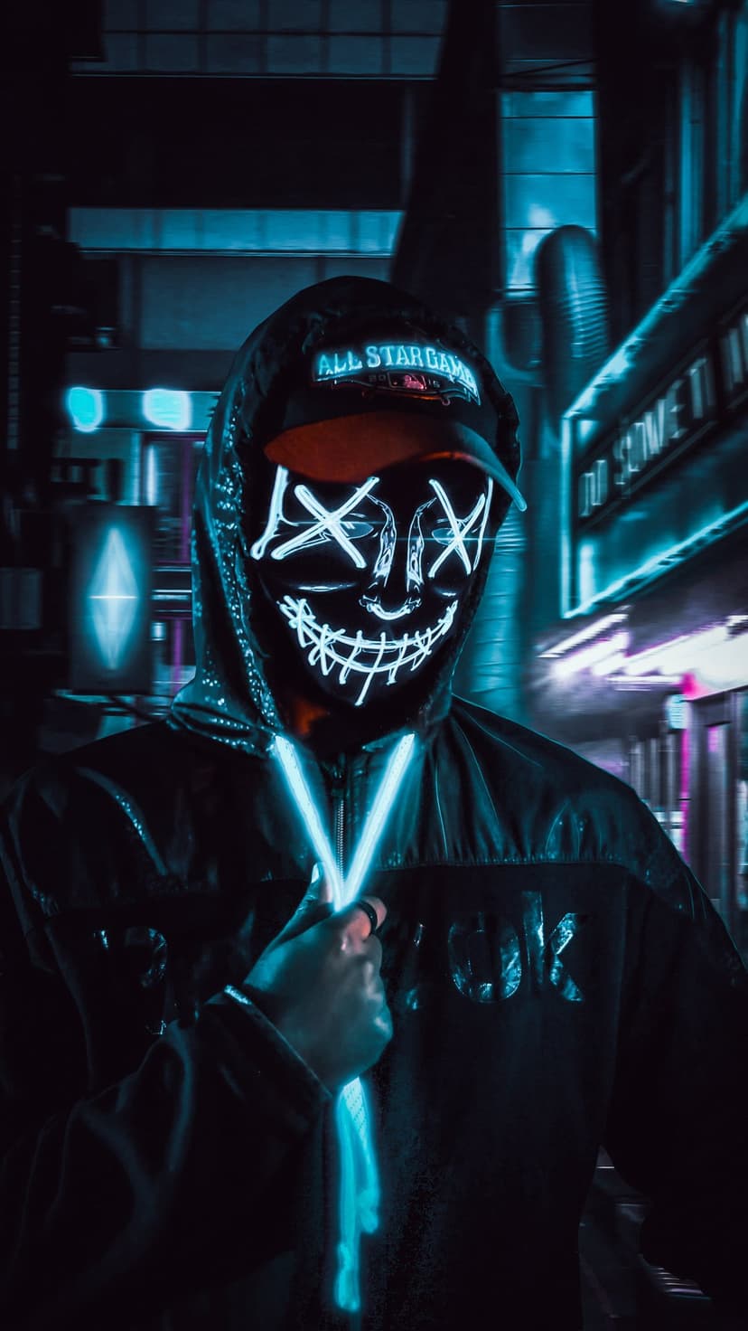 Masked figure in a dark hoodie with glowing blue X-eyes and a grinning mouth against blurred urban city lights.