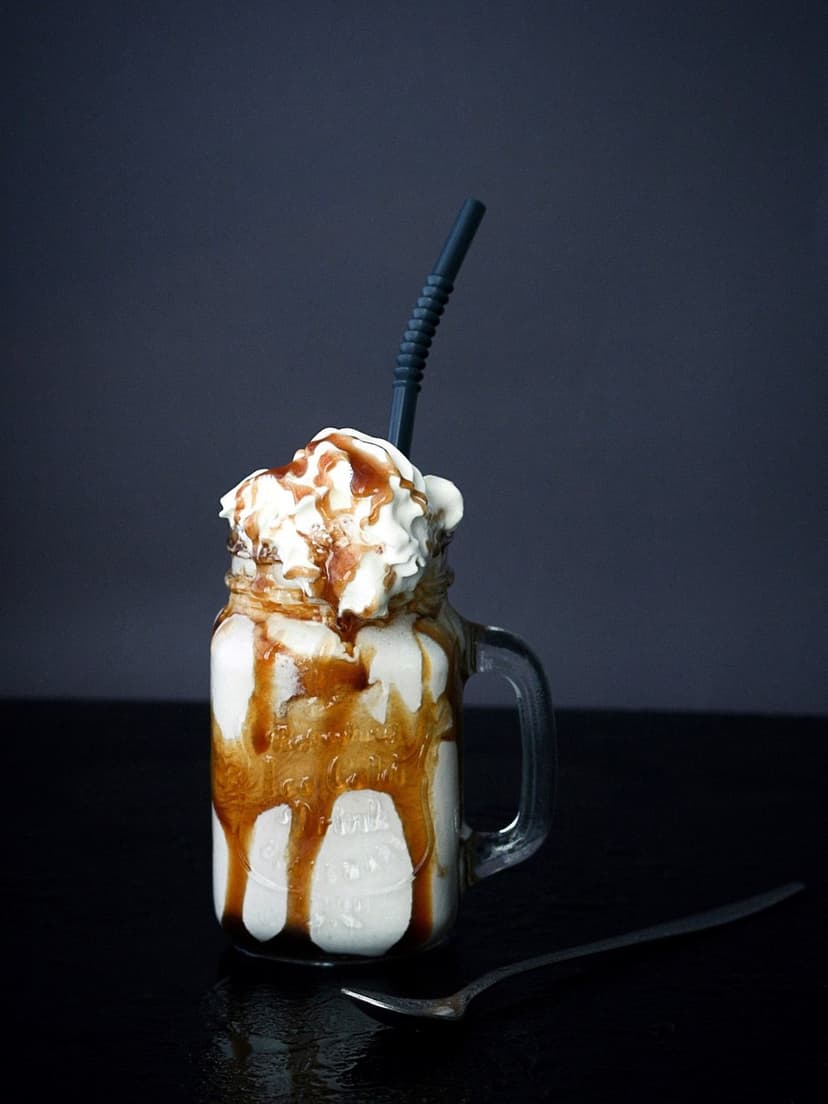 Caramel milkshake in a mason jar featuring thick whipped cream, golden syrup drizzle, and a single dark straw.