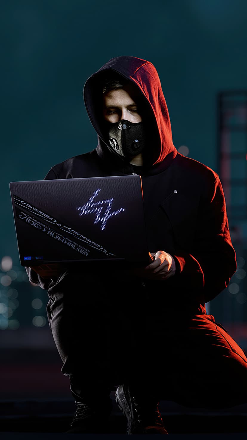 Alan Walker in a black mask and hoodie holds a glowing ROG laptop with a neon logo against a city dusk backdrop.