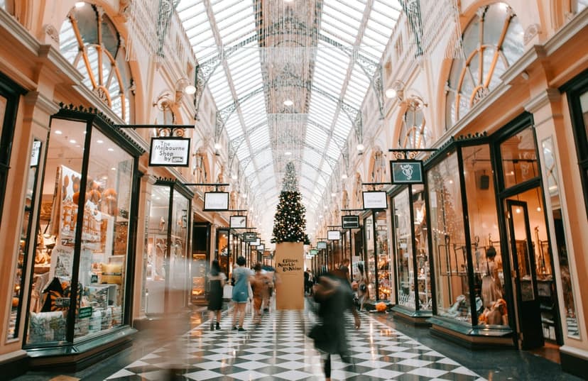 Decorated Christmas tree stands in a historic shopping arcade with a glass ceiling and checkered tile flooring.