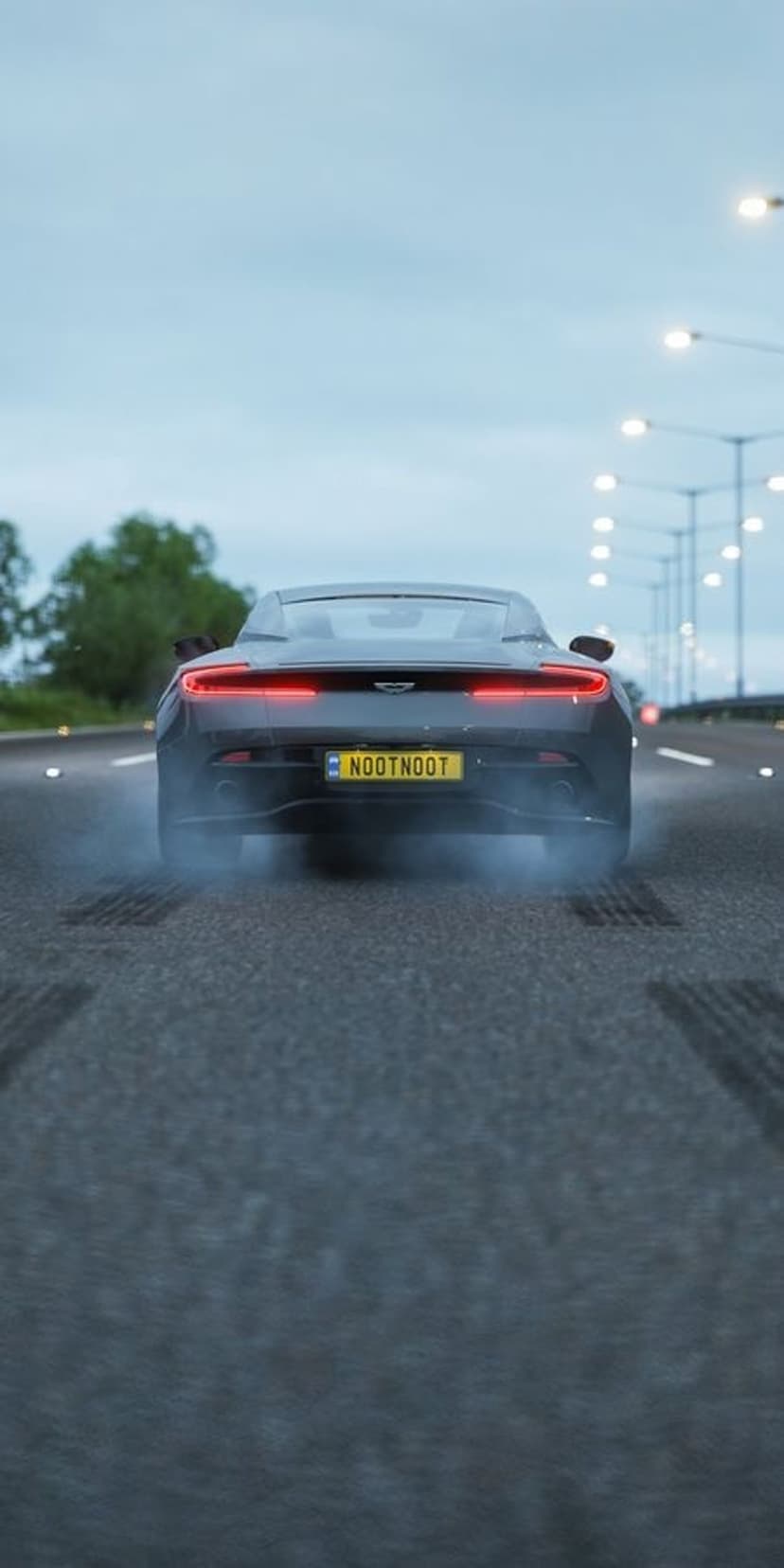Aston Martin sports car drifting on a wet road at night with glowing red taillights and thick tire smoke.