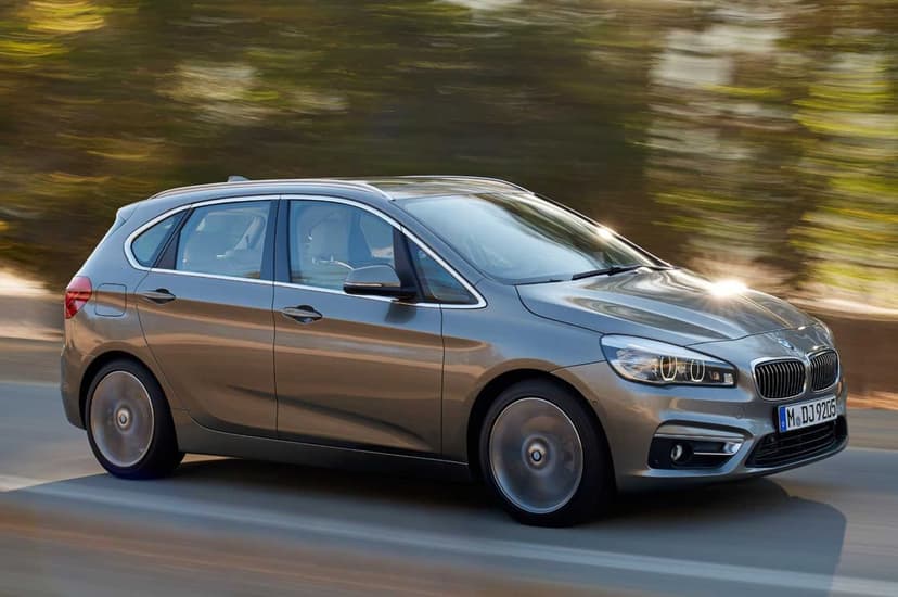 Silver BMW hatchback driving fast on a sunlit road with motion blurred trees and a bright lens flare.