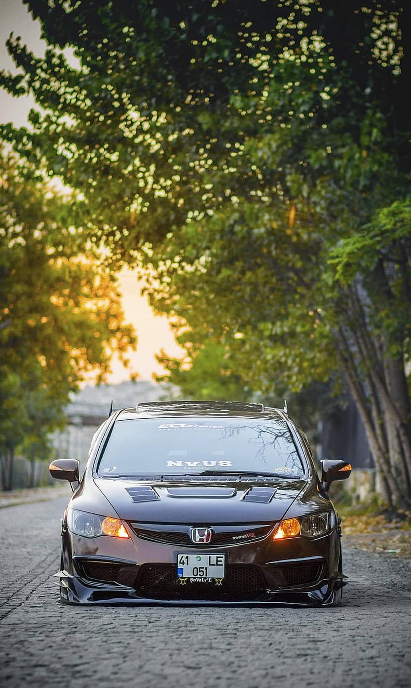 Dark brown Honda Civic Type R with a front splitter parked on a cobblestone road during a warm golden hour sunset.