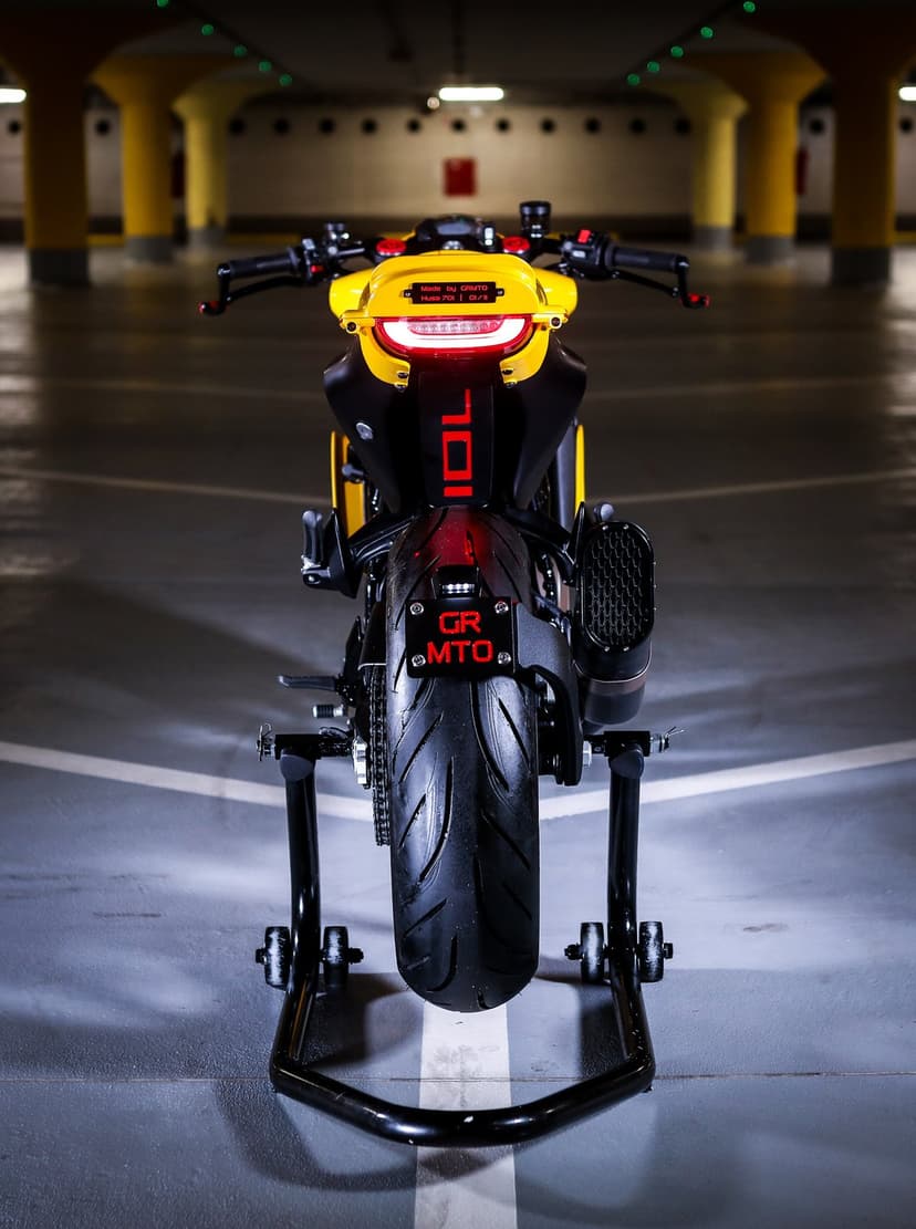 Rear view of a yellow custom motorcycle with glowing red lights on a stand in a parking garage.