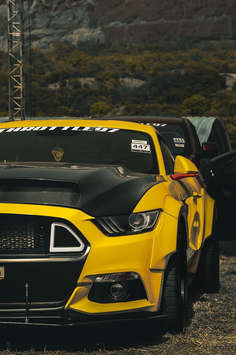 Yellow Ford Mustang with a black performance hood and wide body kit captured in a vertical automotive shot.