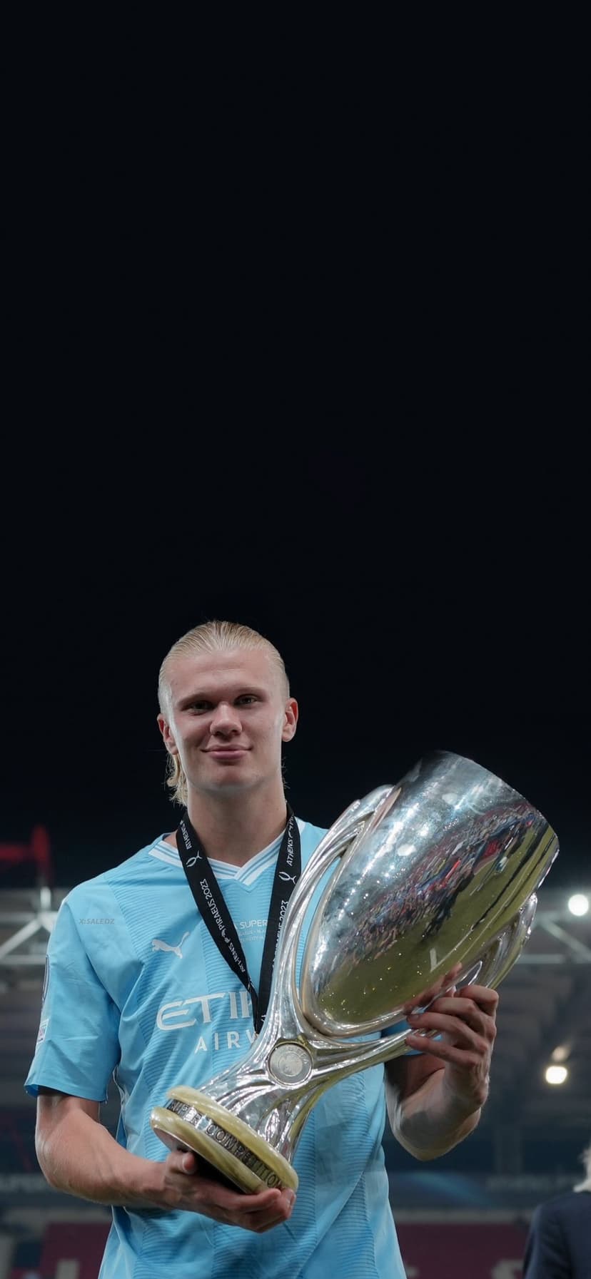 Erling Haaland smiles while holding the silver Super Cup trophy wearing a light blue Manchester City jersey.