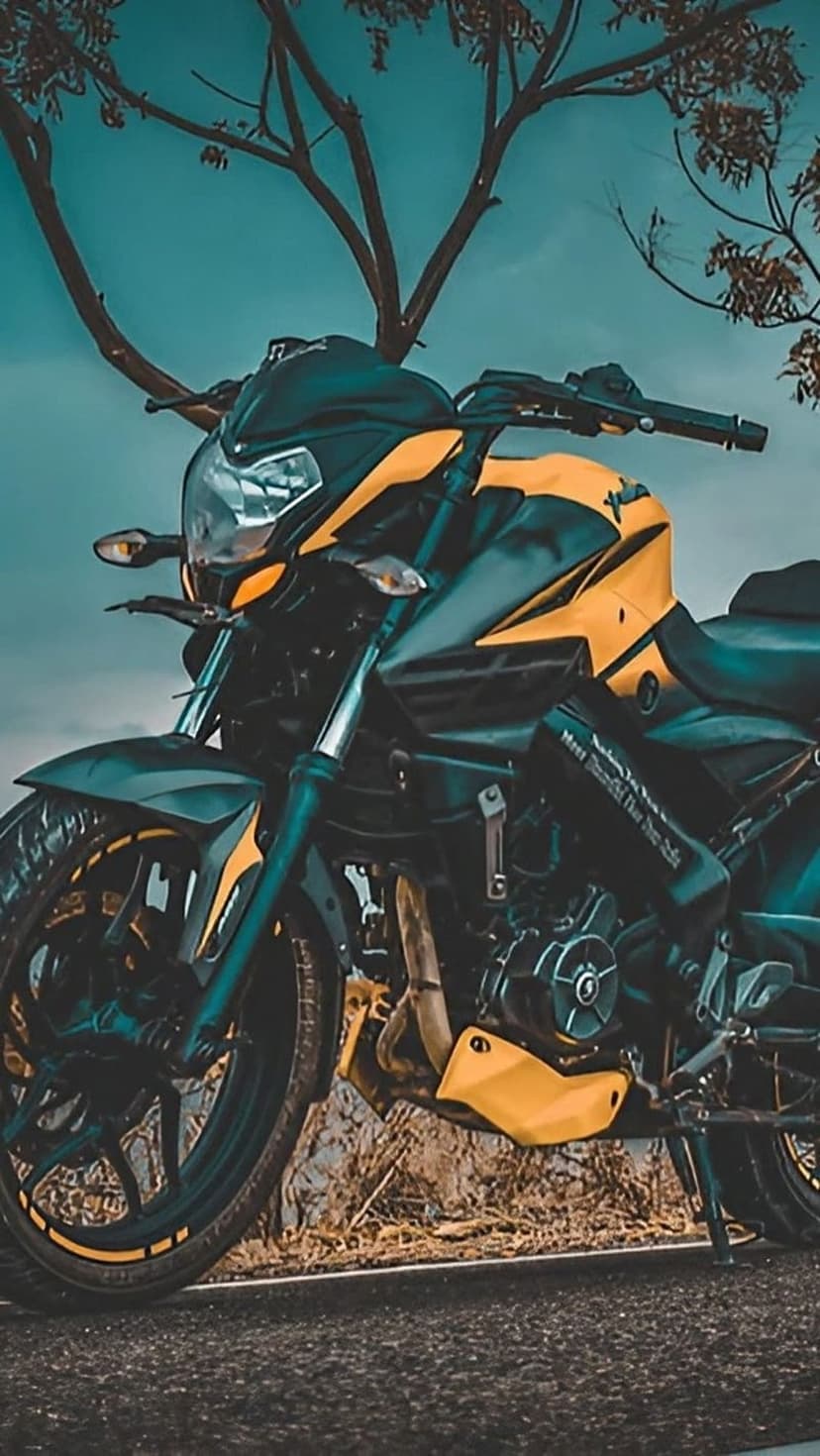 Yellow and black sports motorcycle parked on a road beneath bare tree limbs against a dark blue evening sky.