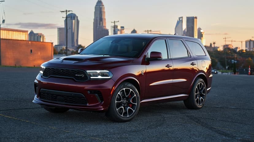 Maroon Dodge Durango SRT Hellcat parked on asphalt with a glowing city skyline in the background at sunset.