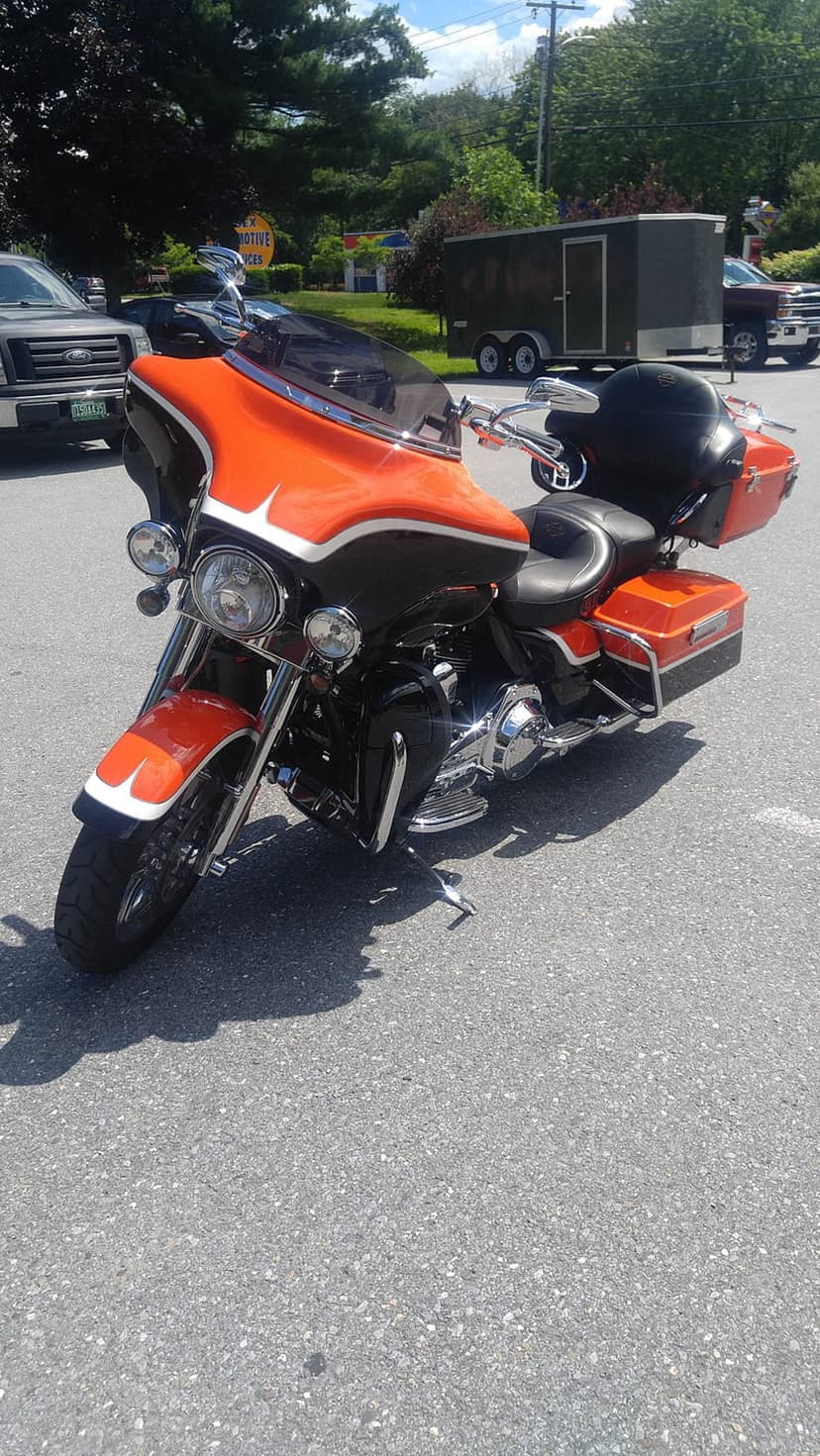 Orange and black Harley Davidson motorcycle parked on asphalt with a black helmet resting on the passenger seat.