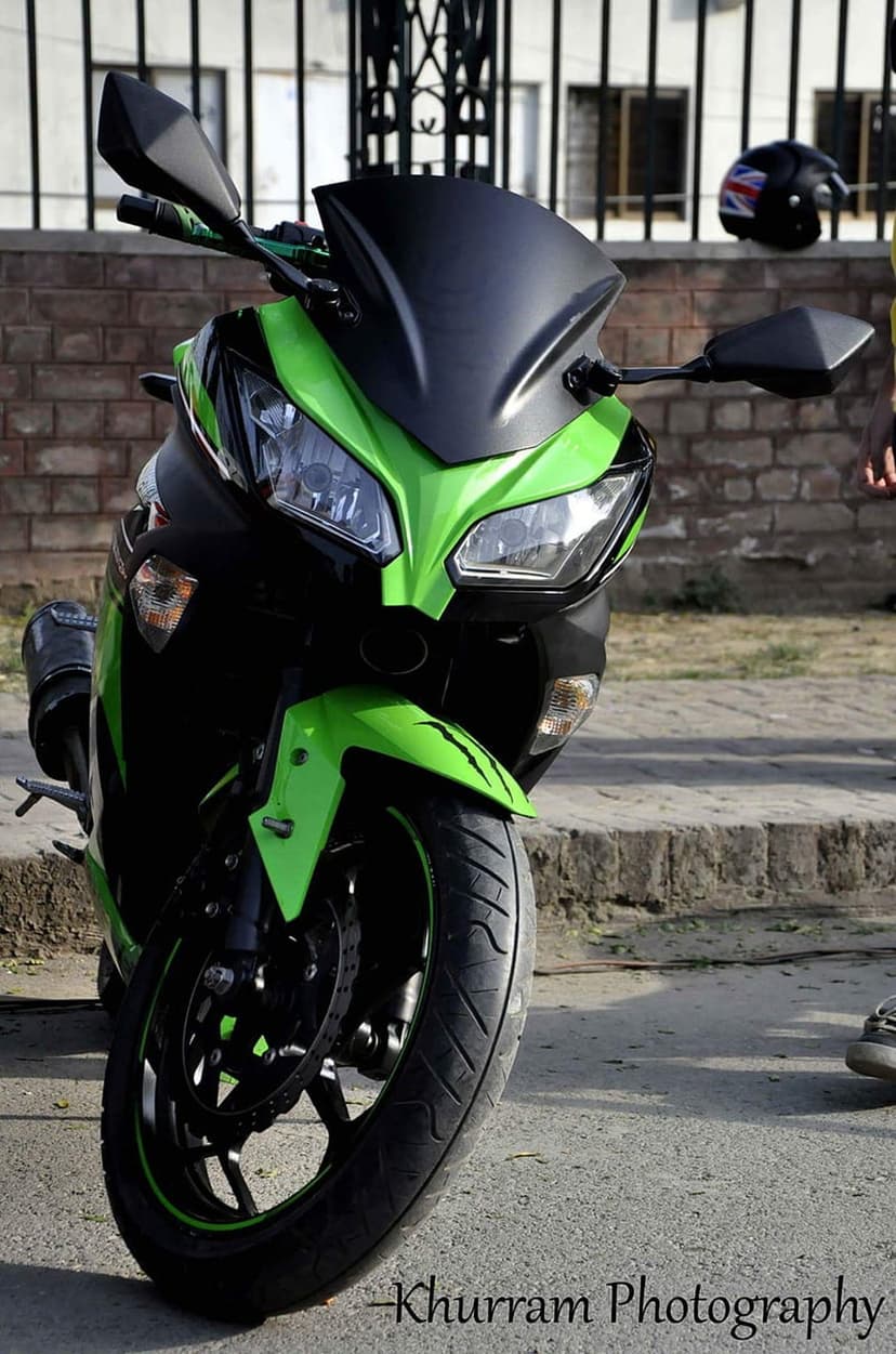Lime green sportbike with a black windscreen stands before a brick wall and a Union Jack helmet in urban light.