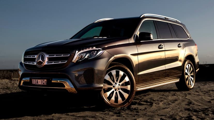Dark grey Mercedes SUV parked on textured sand under golden sunset light with detailed alloy wheels.