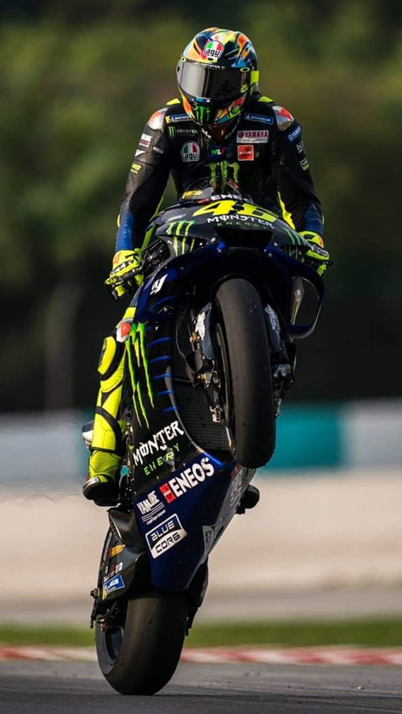 Valentino Rossi performs a high wheelie on a blue Yamaha racing motorcycle during a professional MotoGP event.