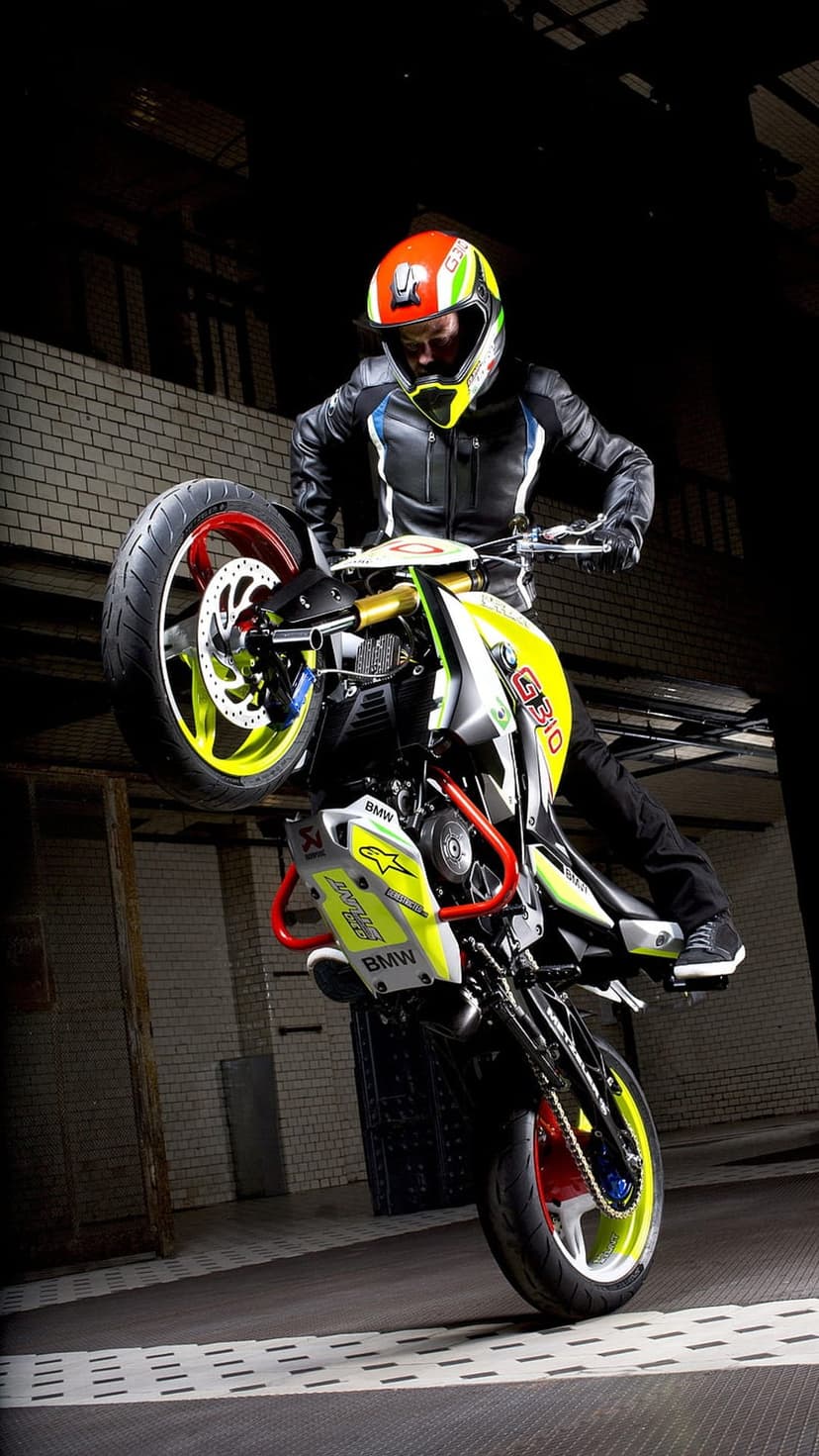 Motorcyclist in a vibrant helmet balances a custom BMW bike on its rear wheel during a daring vertical stunt.