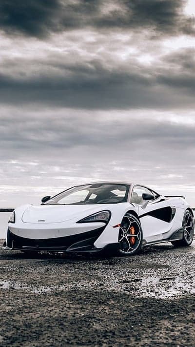 White McLaren sports car parked by a lake under cloudy skies