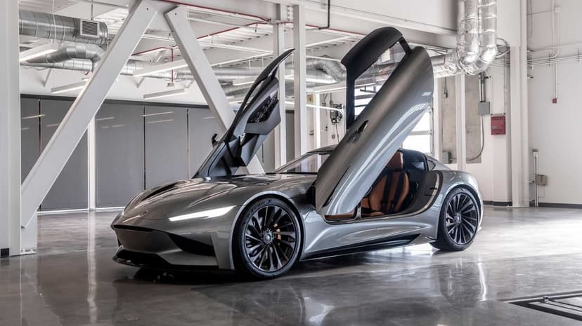 Silver concept car with open butterfly doors in a bright industrial studio with tan leather seats.