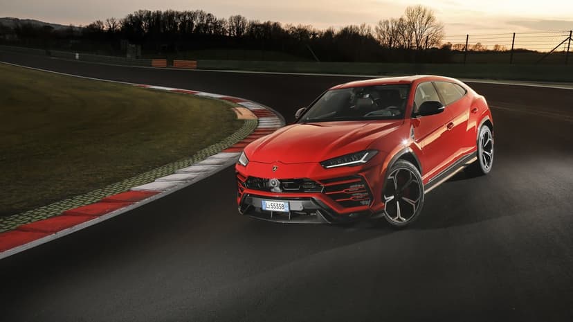 Red Lamborghini Urus on a curved racetrack at sunset with green grass and distant trees in the background.