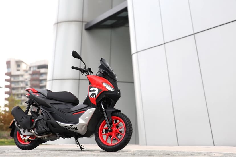 Red Aprilia SR GT scooter with bright red wheels parked in front of a minimalist gray metallic building.