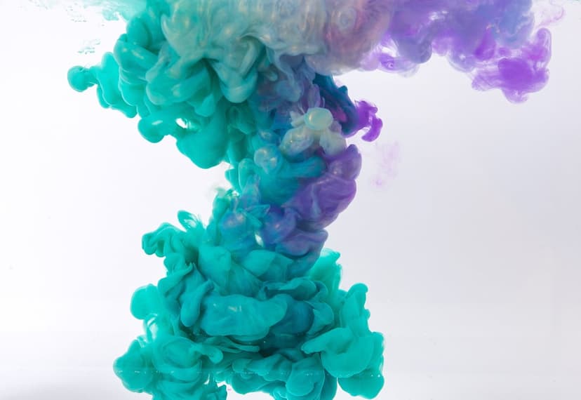 Turquoise and purple ink swirls mix in water against a white background, creating wispy, fluid cloud patterns.